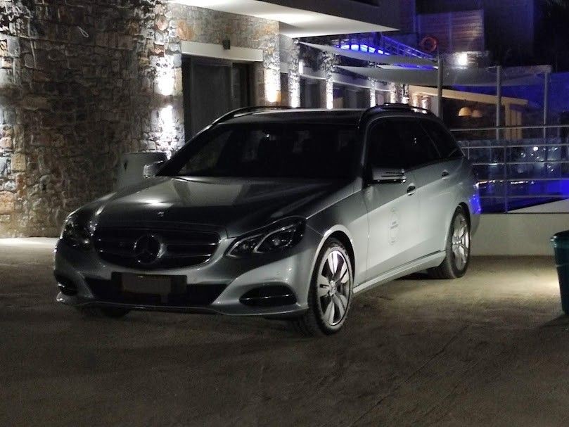 Luxury silver car parked in front of a modern stone building with ambient lighting at night.